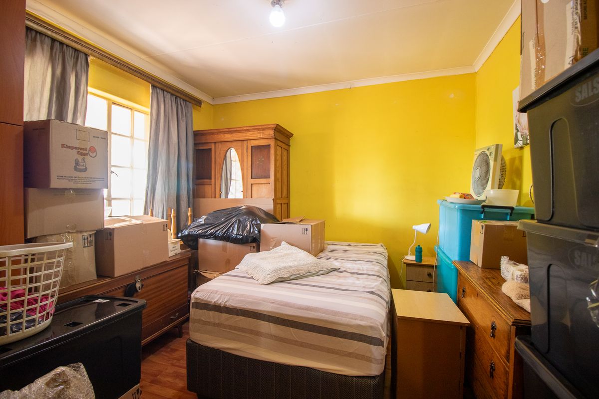 A bedroom featuring laminate flooring and a window with curtains, currently used for storage with various boxes and furniture items.