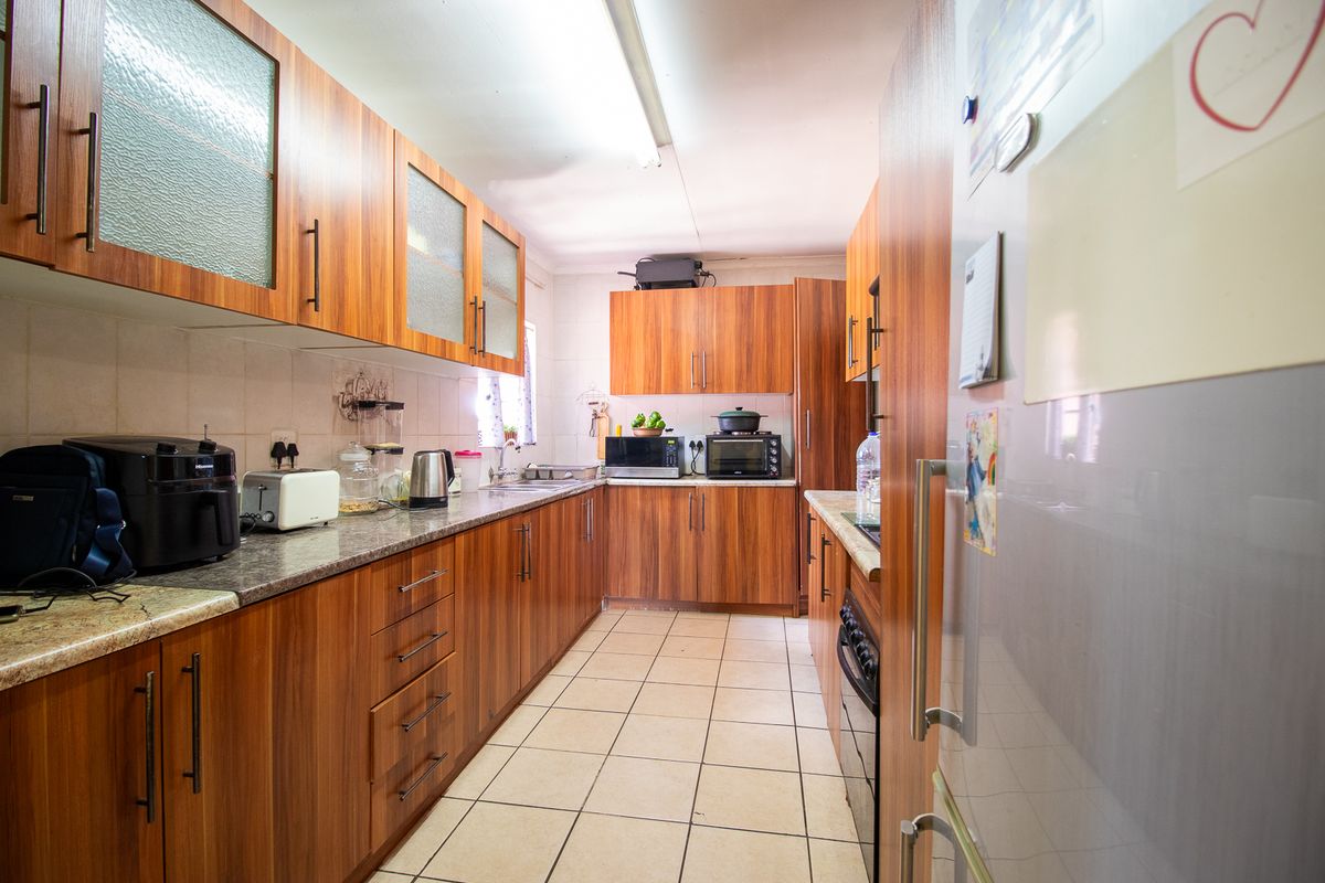 A functional galley-style kitchen featuring wood-look laminate cabinetry, granite countertops, tiled flooring, and a tiled backsplash.
