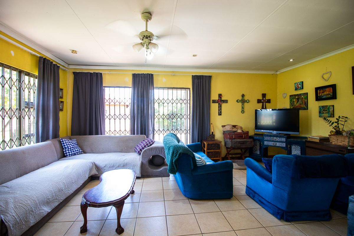 Spacious living room featuring tiled flooring, ceiling fan, and security gates on windows. The space requires cosmetic updates to the wall finishes.