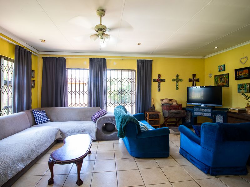 Spacious living room featuring tiled flooring, ceiling fan, and security gates on windows. The space requires cosmetic updates to the wall finishes.