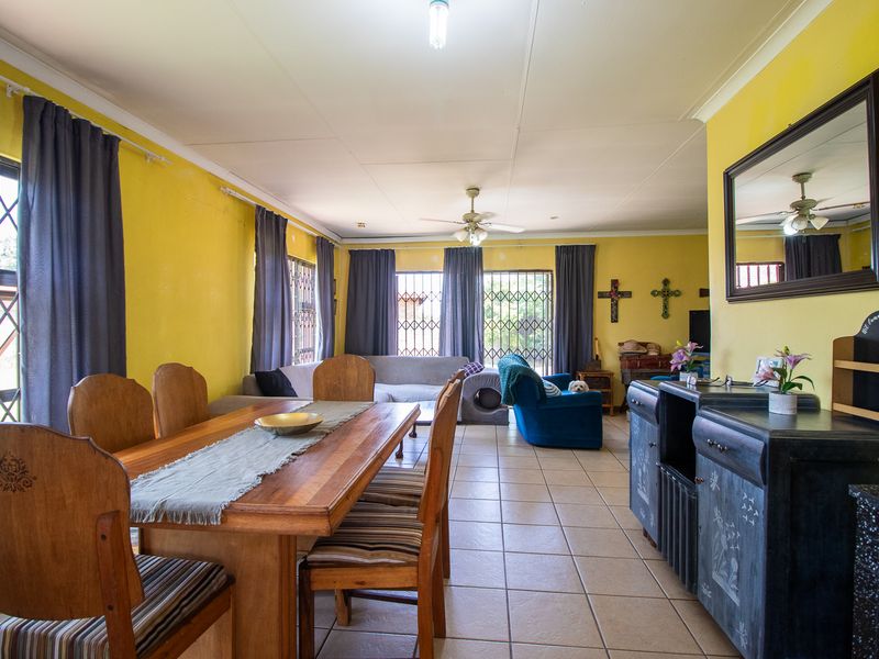 Open-plan living and dining area featuring tiled flooring, ceiling fan, and security gates on windows, with potential for cosmetic updates.