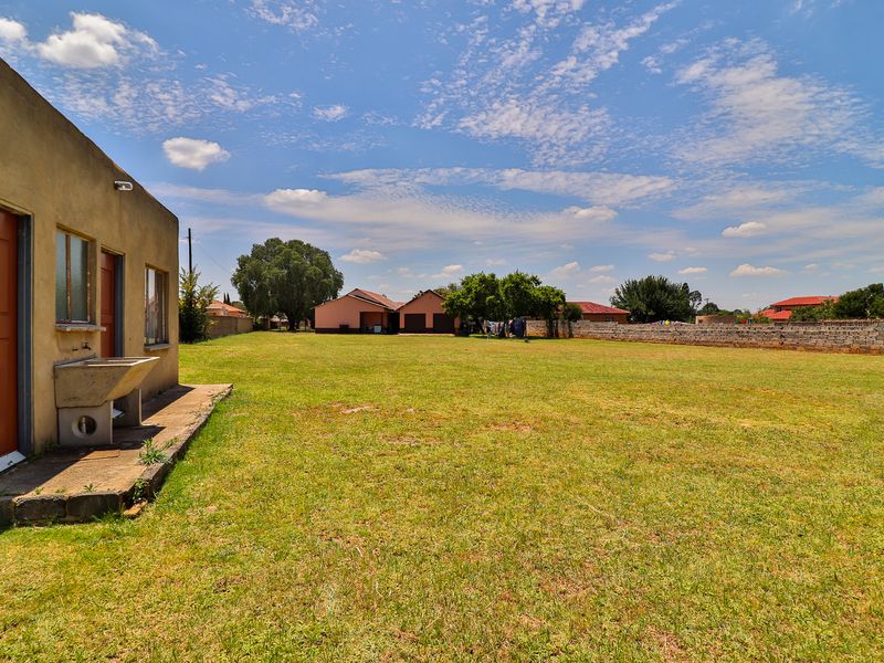 Spacious rear yard featuring a large grass lawn, a concrete wash basin attached to the building, and a perimeter brick boundary wall.