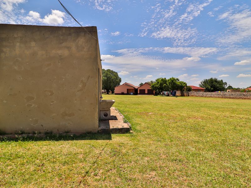A spacious backyard area featuring a large lawn, a perimeter boundary wall, and a functional exterior utility sink attached to the side of the structure.
