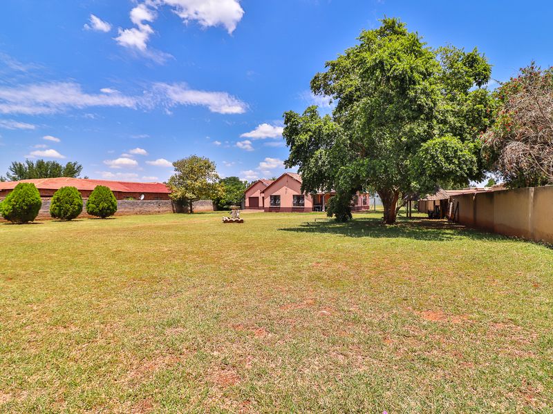 A spacious, well-maintained garden featuring a large lawn, mature trees, and a secure perimeter wall surrounding the property.