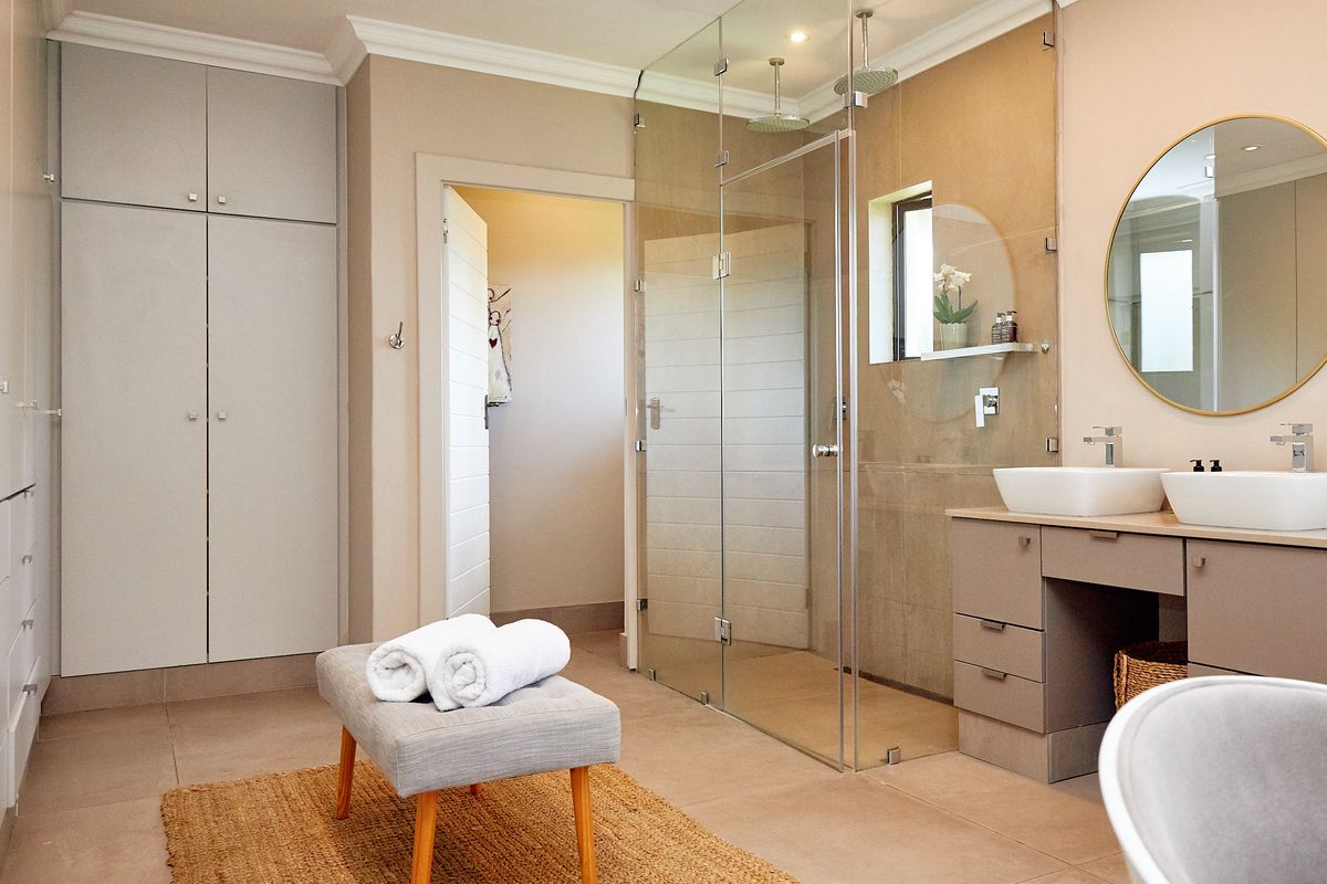 Modern bathroom featuring a double vanity, spacious glass-enclosed shower with dual rainfall heads, and ample built-in storage cabinetry.