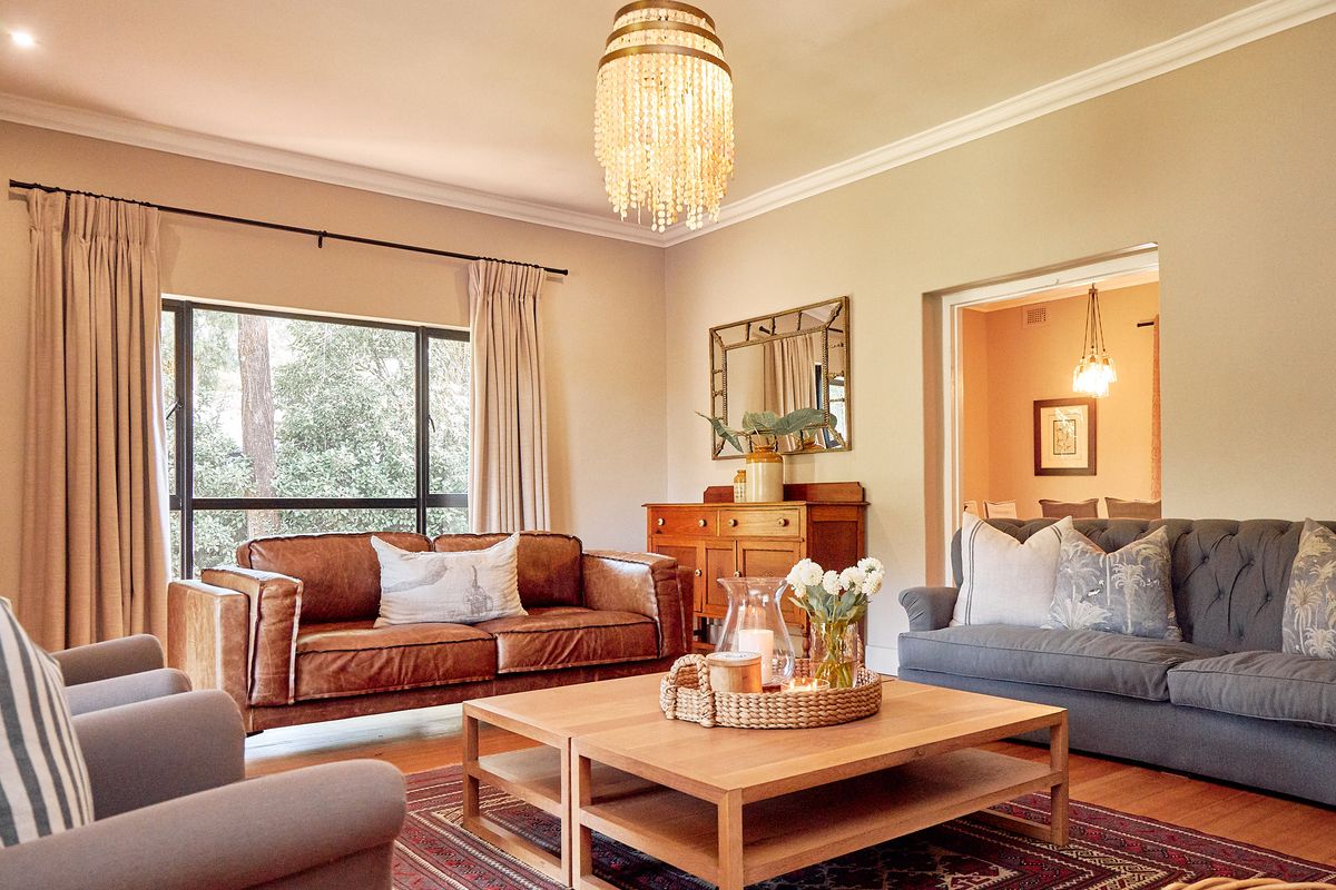 A well-maintained living room featuring hardwood flooring, crown molding, and large windows that provide natural light and garden views.
