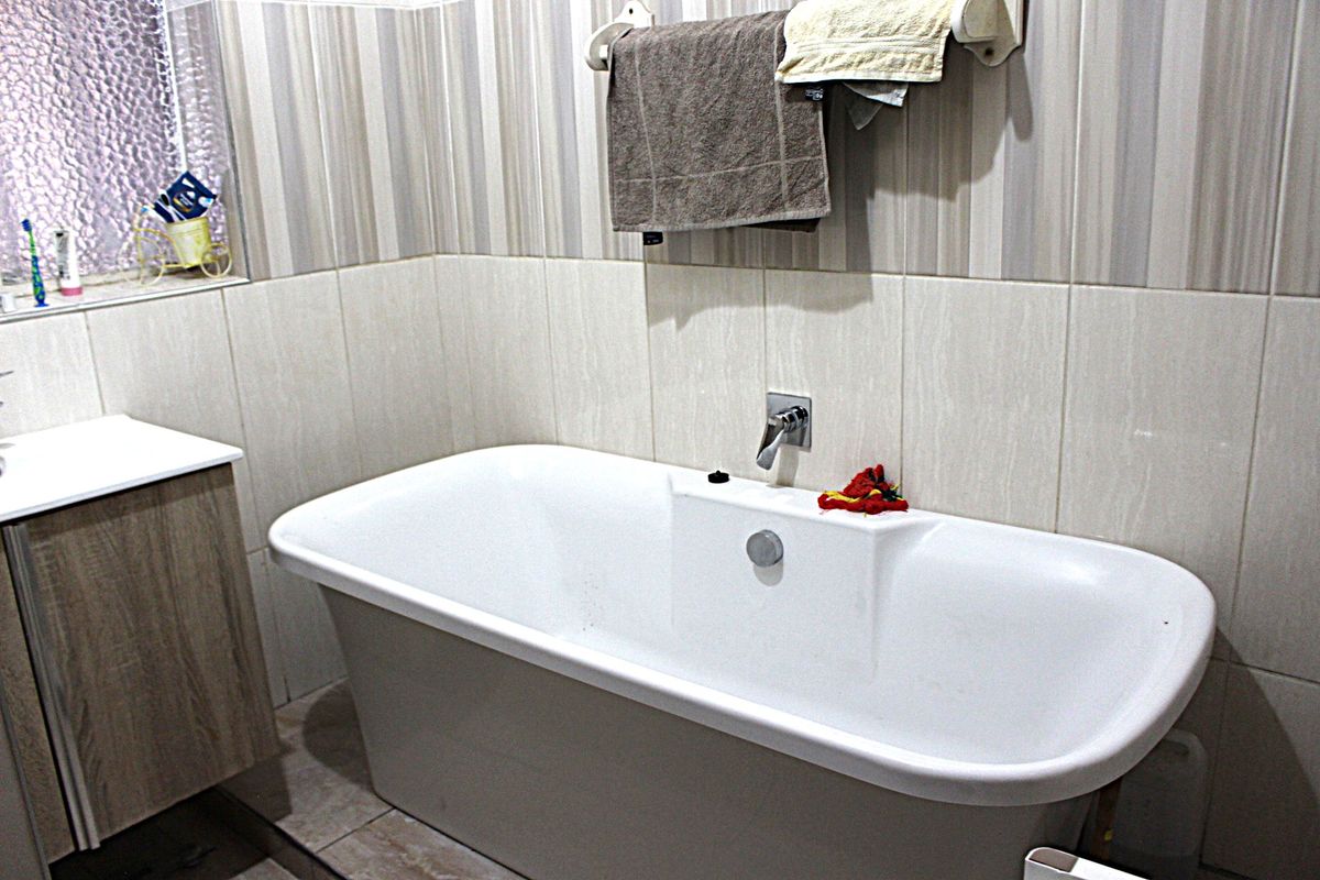 A functional bathroom featuring a modern freestanding bathtub, wall-mounted mixer tap, and a vanity cabinet with neutral-toned wall tiling.
