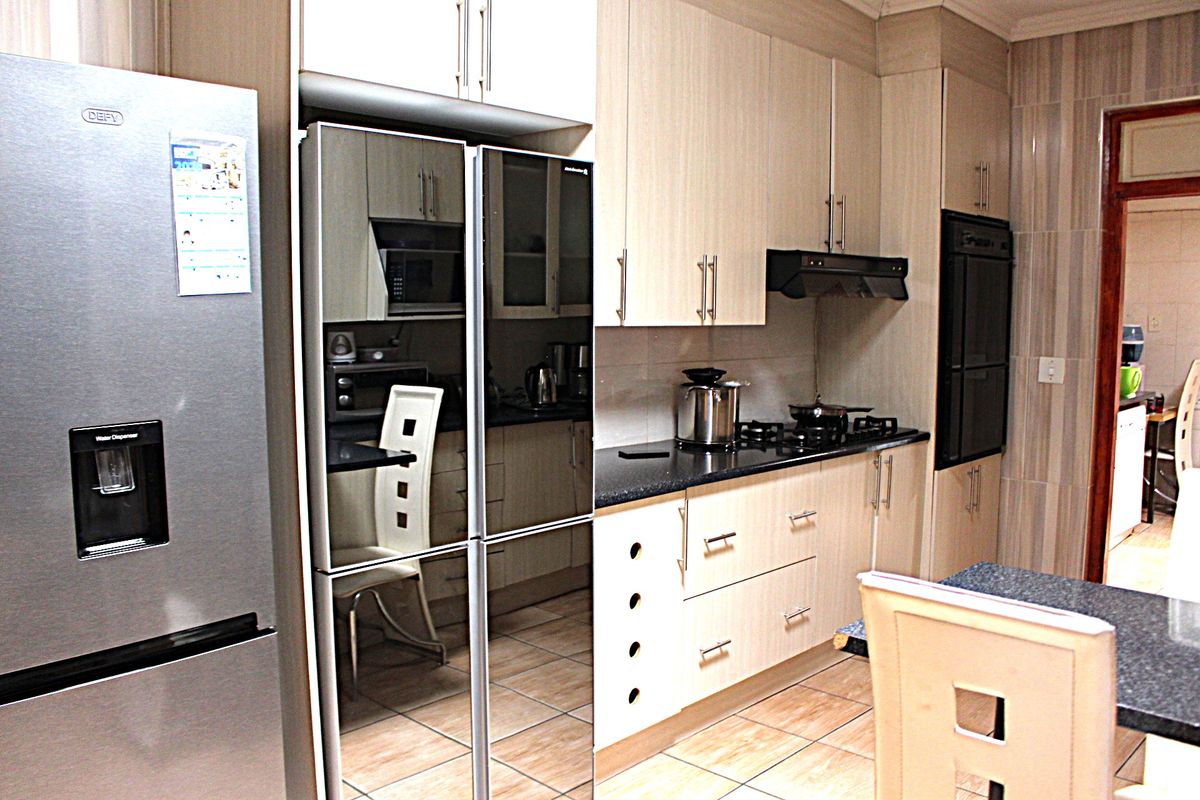 A functional kitchen featuring light wood cabinetry, granite countertops, a gas hob, extractor fan, and built-in oven with tiled finishes throughout.