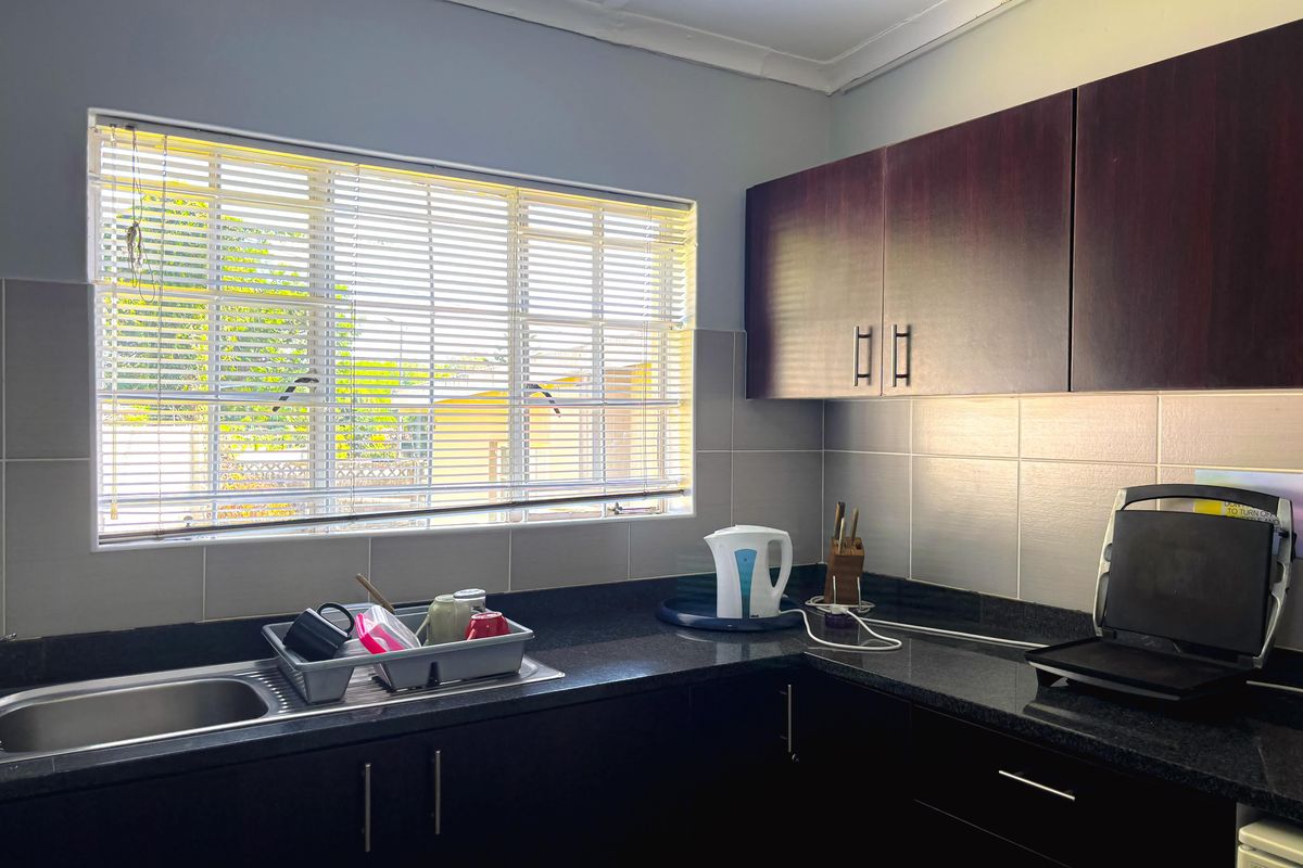 A functional kitchen featuring dark wood cabinetry, granite countertops, a stainless steel sink, and a tiled backsplash with natural light from the window.