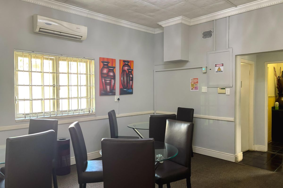 A functional living area featuring crown molding, chair rail detailing, a wall-mounted air conditioning unit, and security bars on the window.
