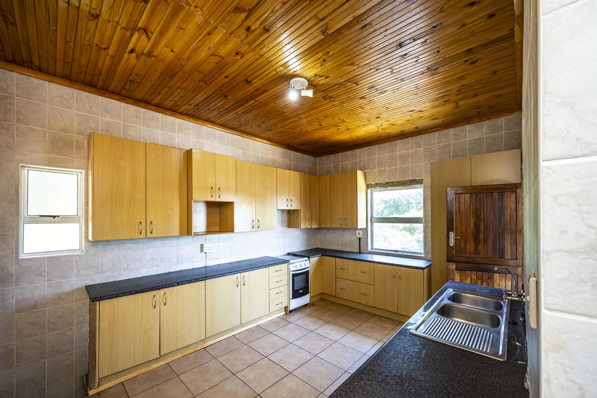 A functional kitchen featuring light wood cabinetry, dark countertops, tiled flooring, and a distinctive wooden panelled ceiling.