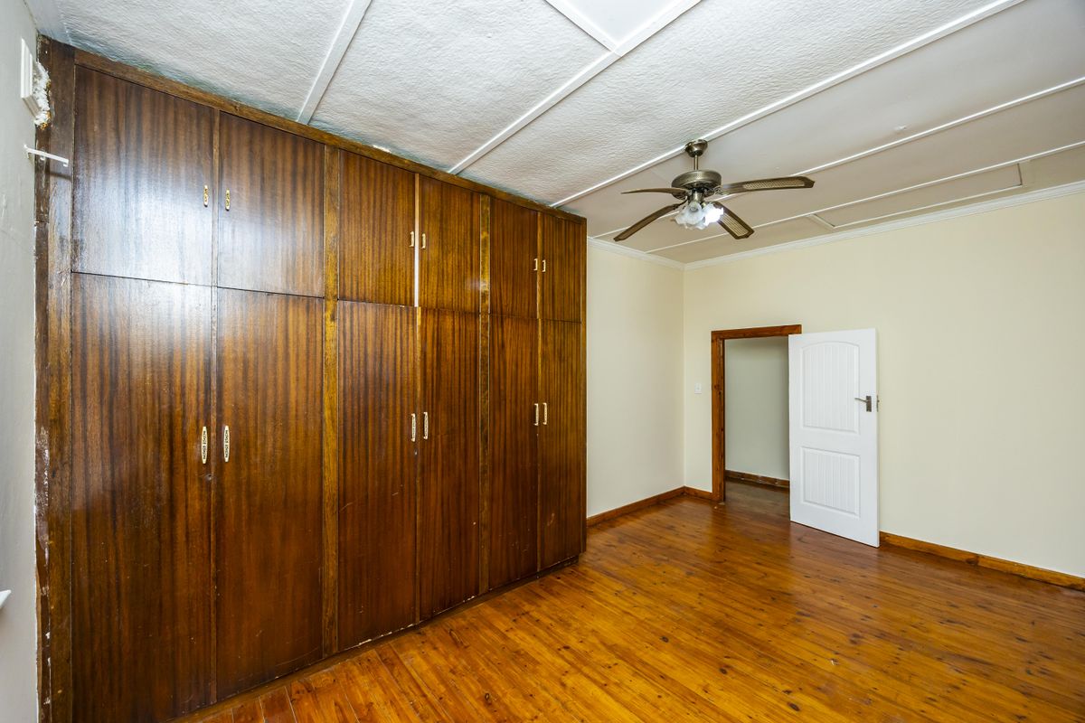 A bedroom featuring polished timber flooring, a large built-in wooden wardrobe, and a ceiling fan.