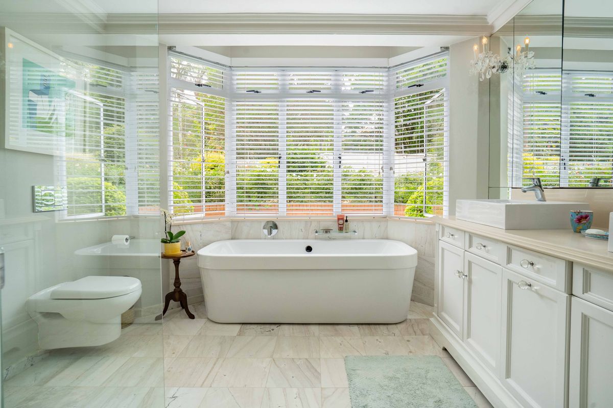 A bright, modern bathroom featuring a freestanding bathtub, marble flooring, a sleek vanity with a vessel sink, and a glass-enclosed shower.