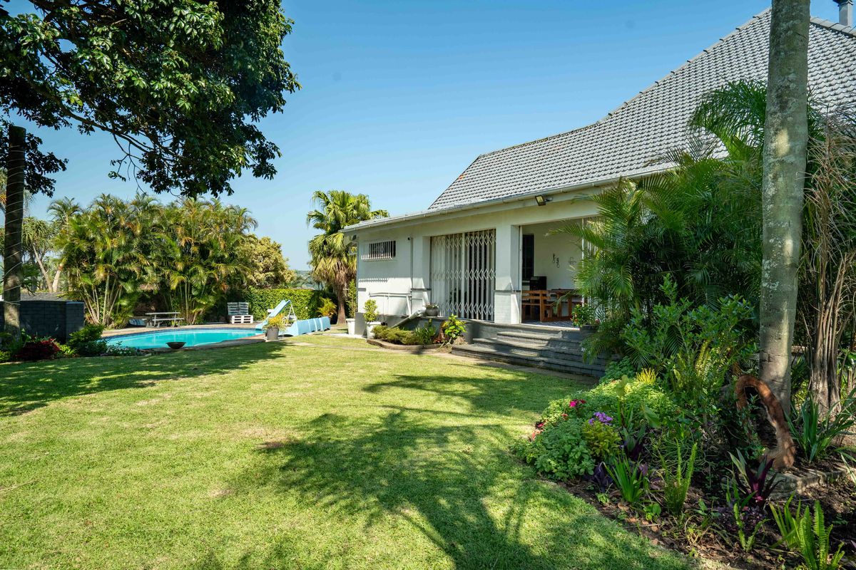 A spacious rear garden featuring a swimming pool, landscaped lawn, and a covered patio area attached to the main house structure.
