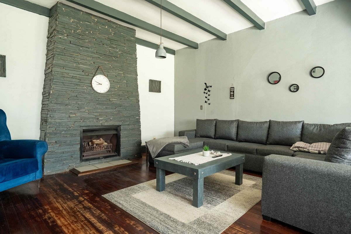 A cozy living room featuring a prominent stone-clad fireplace, exposed ceiling beams, and rich dark hardwood flooring.