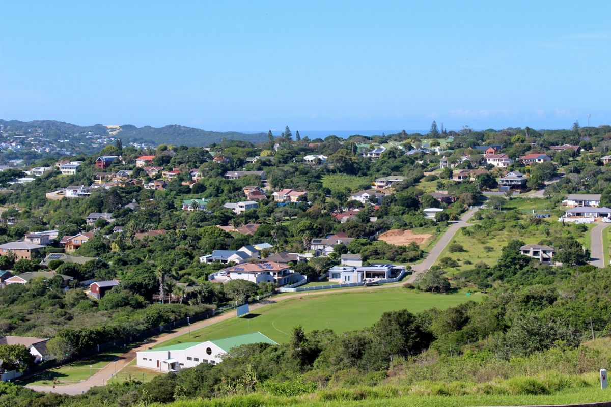 An elevated aerial view of a residential neighborhood featuring lush greenery, paved roads, and surrounding coastal landscape.