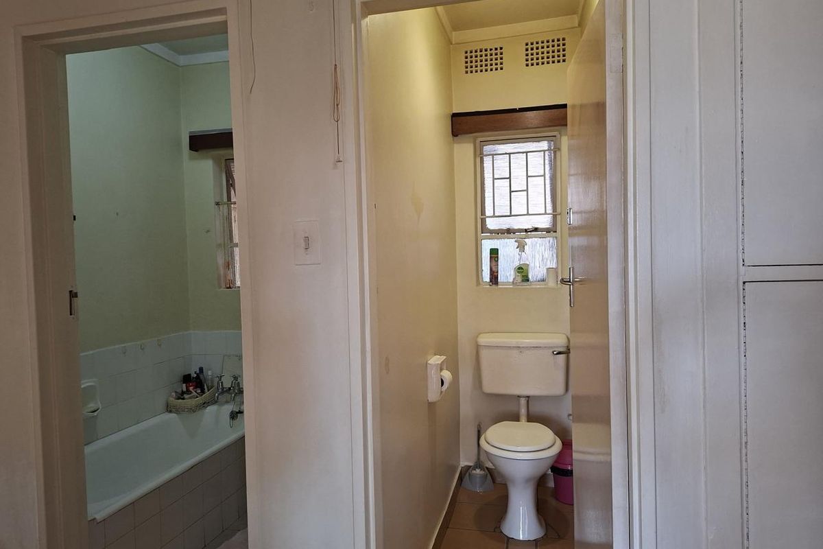 A dated bathroom and separate toilet area featuring original fixtures, tiled flooring, and security bars on the windows.