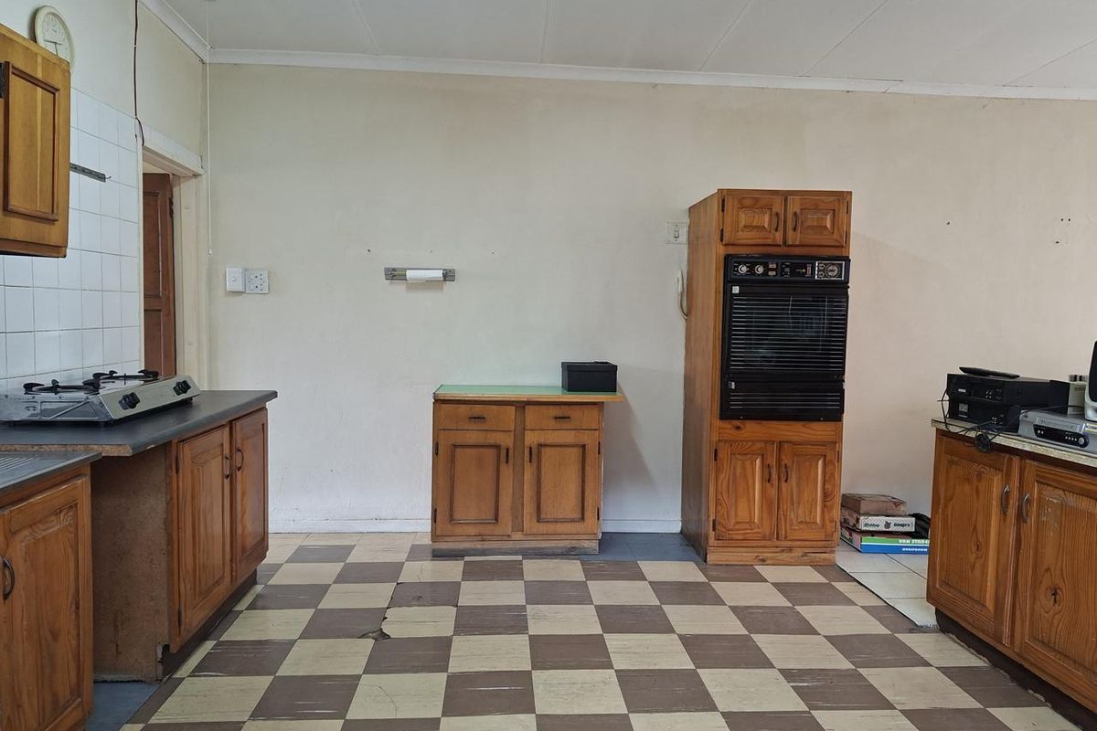 A dated kitchen featuring wooden cabinetry, an integrated eye-level oven, and a checkerboard tiled floor, offering significant potential for modernization and renovation.