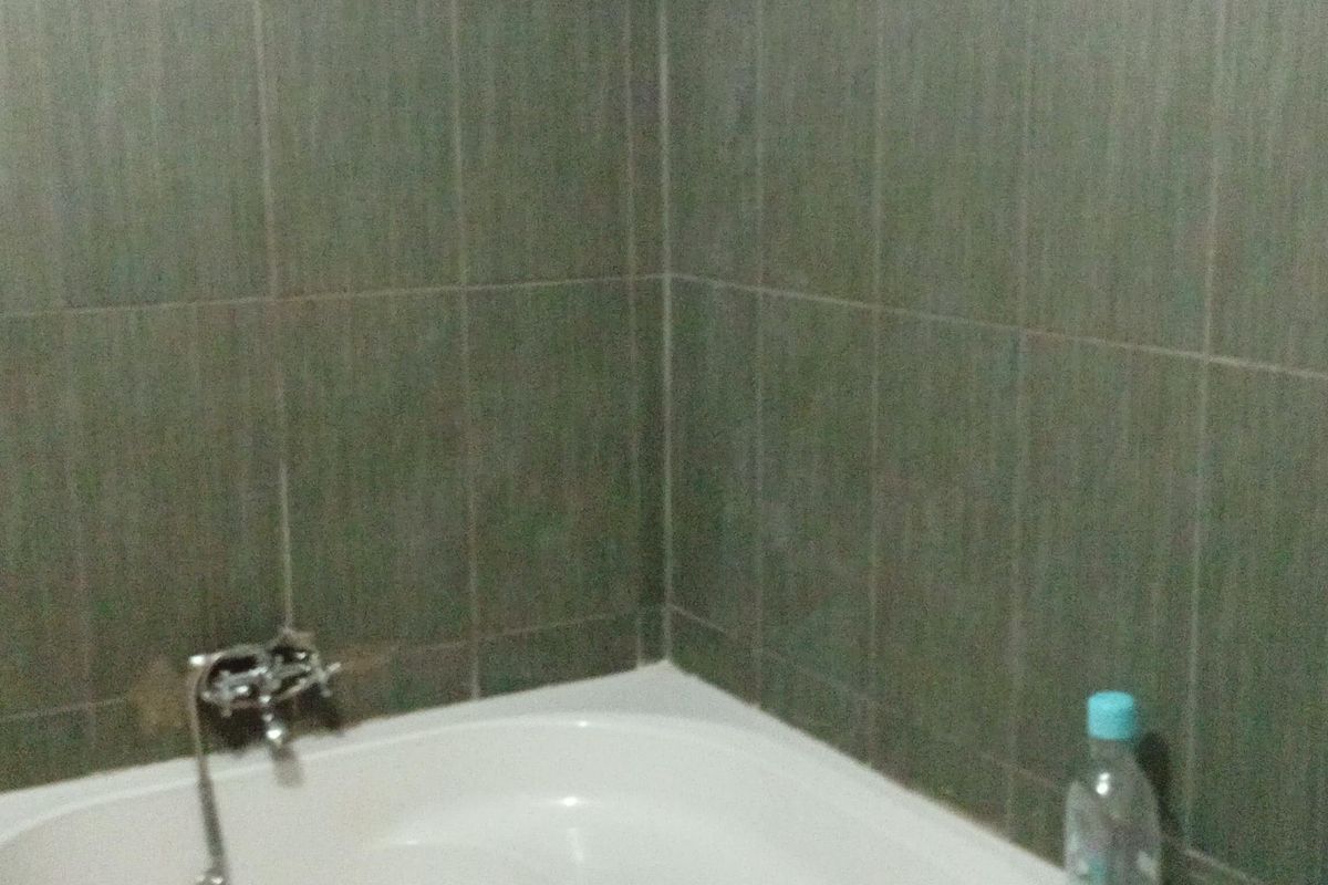 A corner bathtub featuring dark grey wall tiling and chrome fixtures, providing a functional bathing space.
