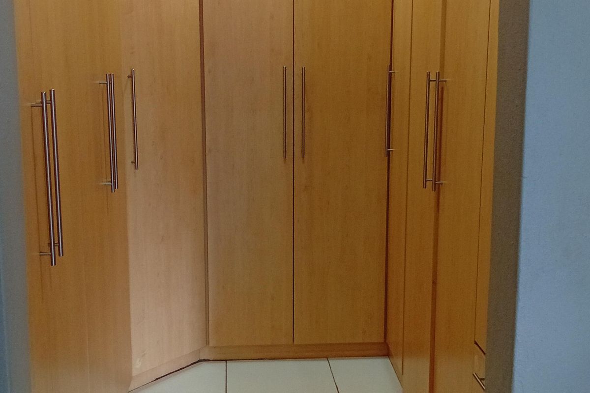 A walk-in closet or dressing area featuring extensive built-in wooden cabinetry with modern handles and tiled flooring.