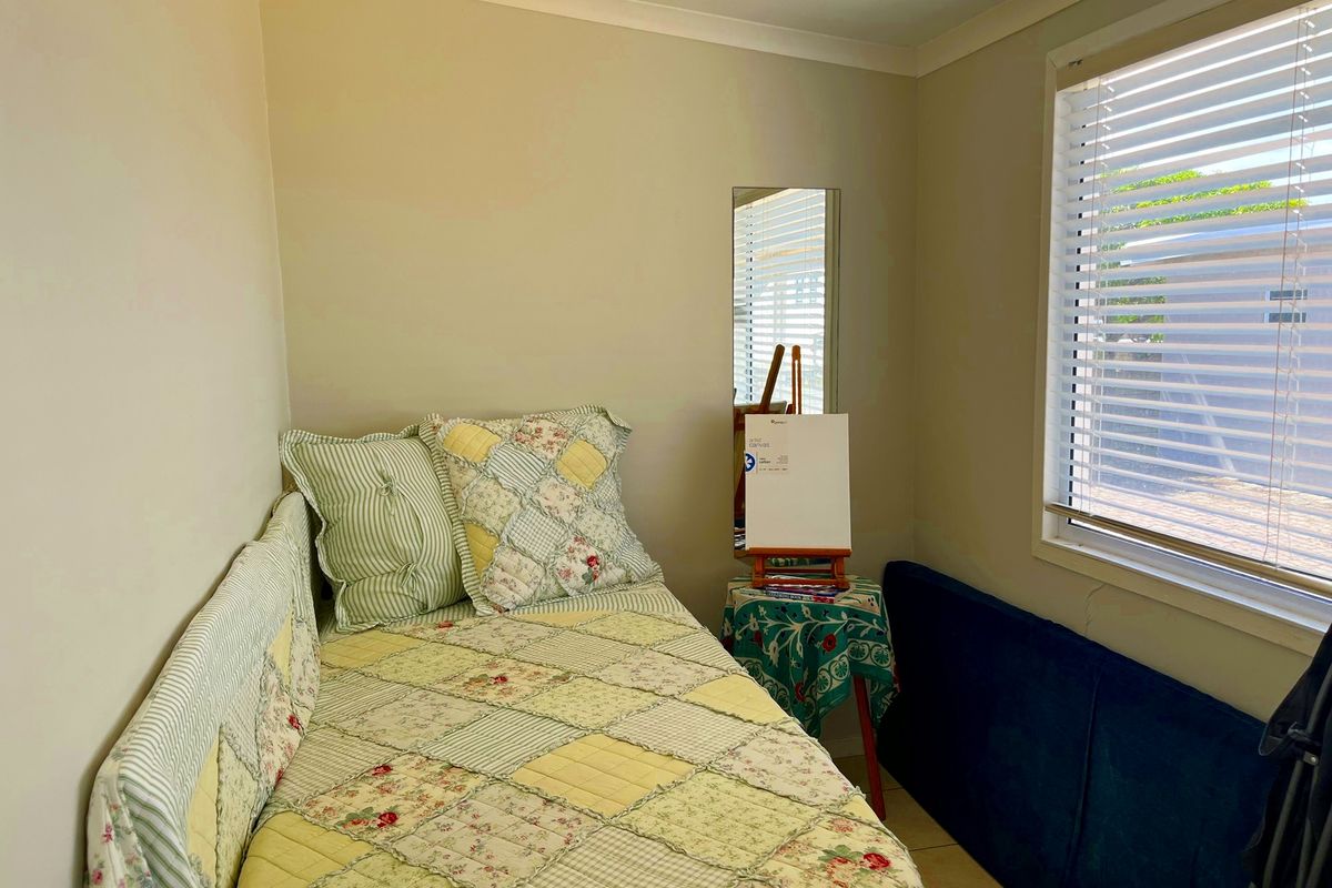 A compact bedroom featuring neutral wall tones, tiled flooring, and a window fitted with venetian blinds.