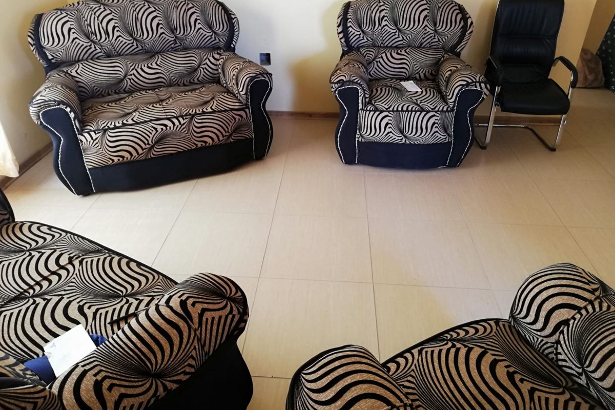 A living room area featuring neutral floor tiling and plain wall finishes, providing a functional space for seating arrangements.