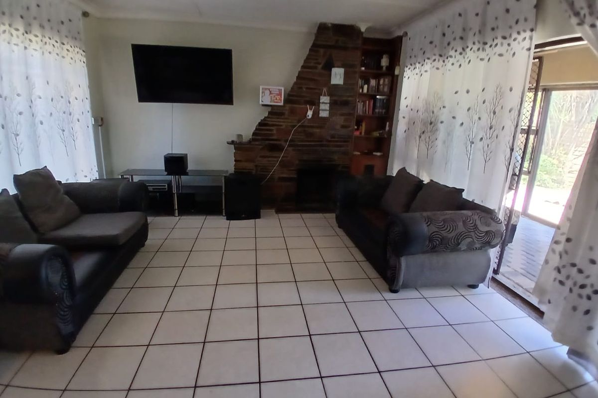 A living room featuring a stone fireplace, built-in shelving, and ceramic floor tiles, offering a functional space with potential for modern updates.