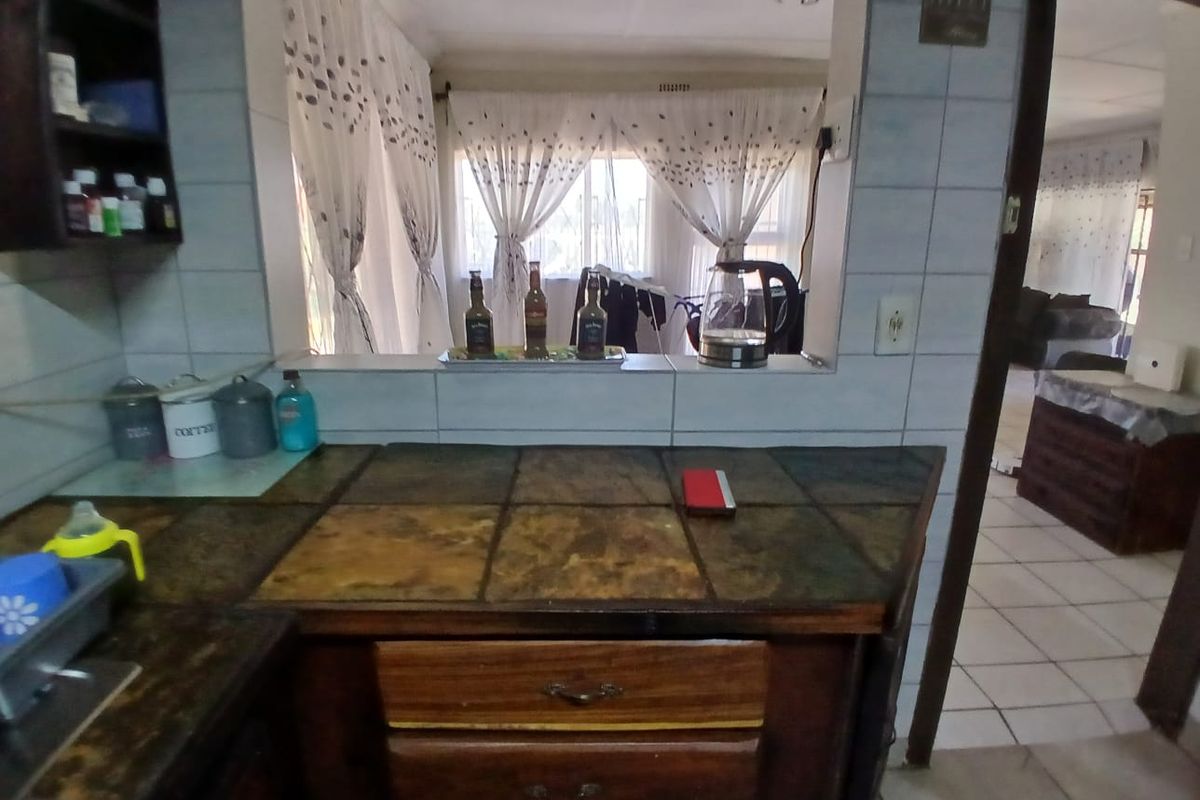 A kitchen featuring tiled countertops and built-in wooden cabinetry with a convenient pass-through window looking into the adjacent living area.