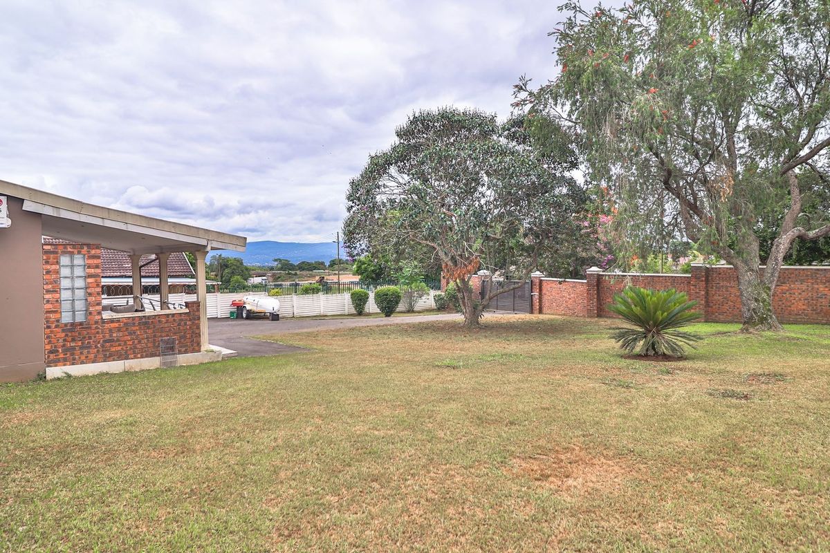 Spacious rear garden featuring a large lawn, mature trees, brick boundary wall, and a covered patio area with an external air conditioning unit.