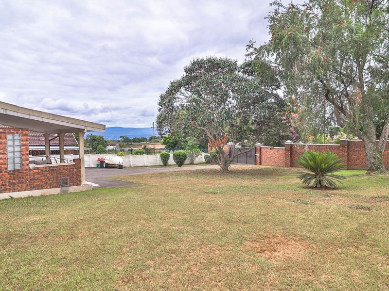 Spacious rear garden featuring a large lawn, mature trees, brick boundary wall, and a covered patio area with an external air conditioning unit.
