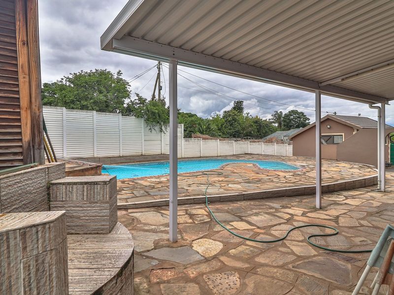 Outdoor pool area featuring a covered patio, stone paved surround, and perimeter fencing, offering a functional space for outdoor relaxation and entertainment.