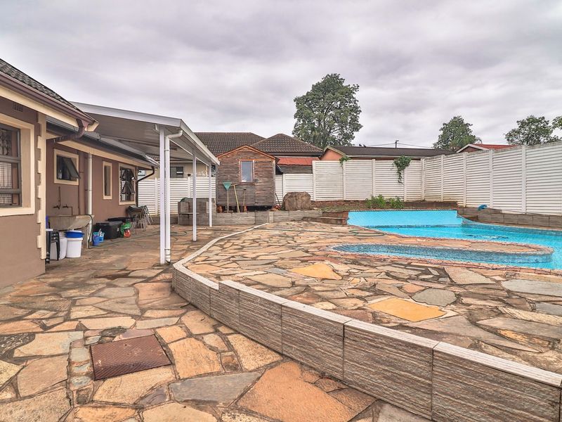 Outdoor pool area featuring stone paving, a covered patio space, and perimeter fencing, providing a functional backyard entertainment zone.