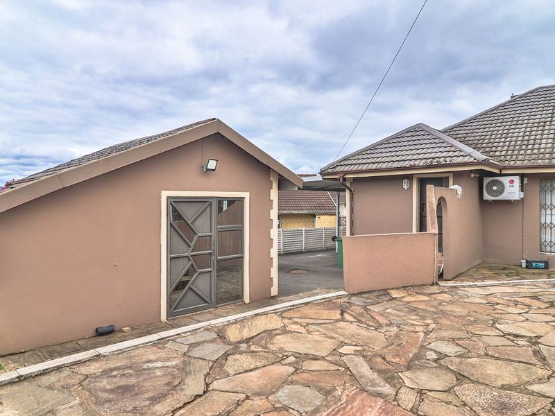 Rear exterior view showing a paved courtyard, a detached structure, and the main house with security features and an external air conditioning unit.