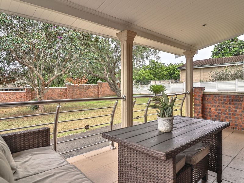 A covered patio featuring tiled flooring, a brick feature wall, and a stainless steel balustrade overlooking the garden.