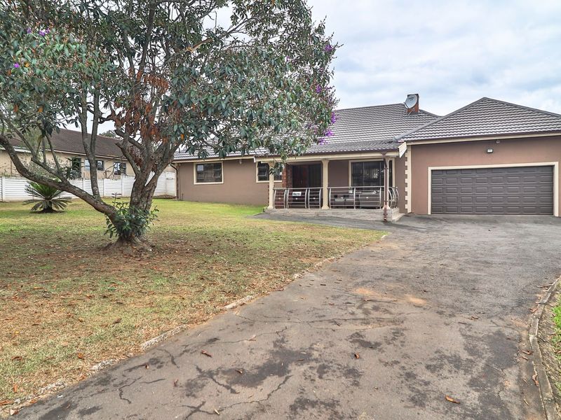 Front view of a single-story house featuring a paved driveway, double garage, and a covered patio area with a large front garden.