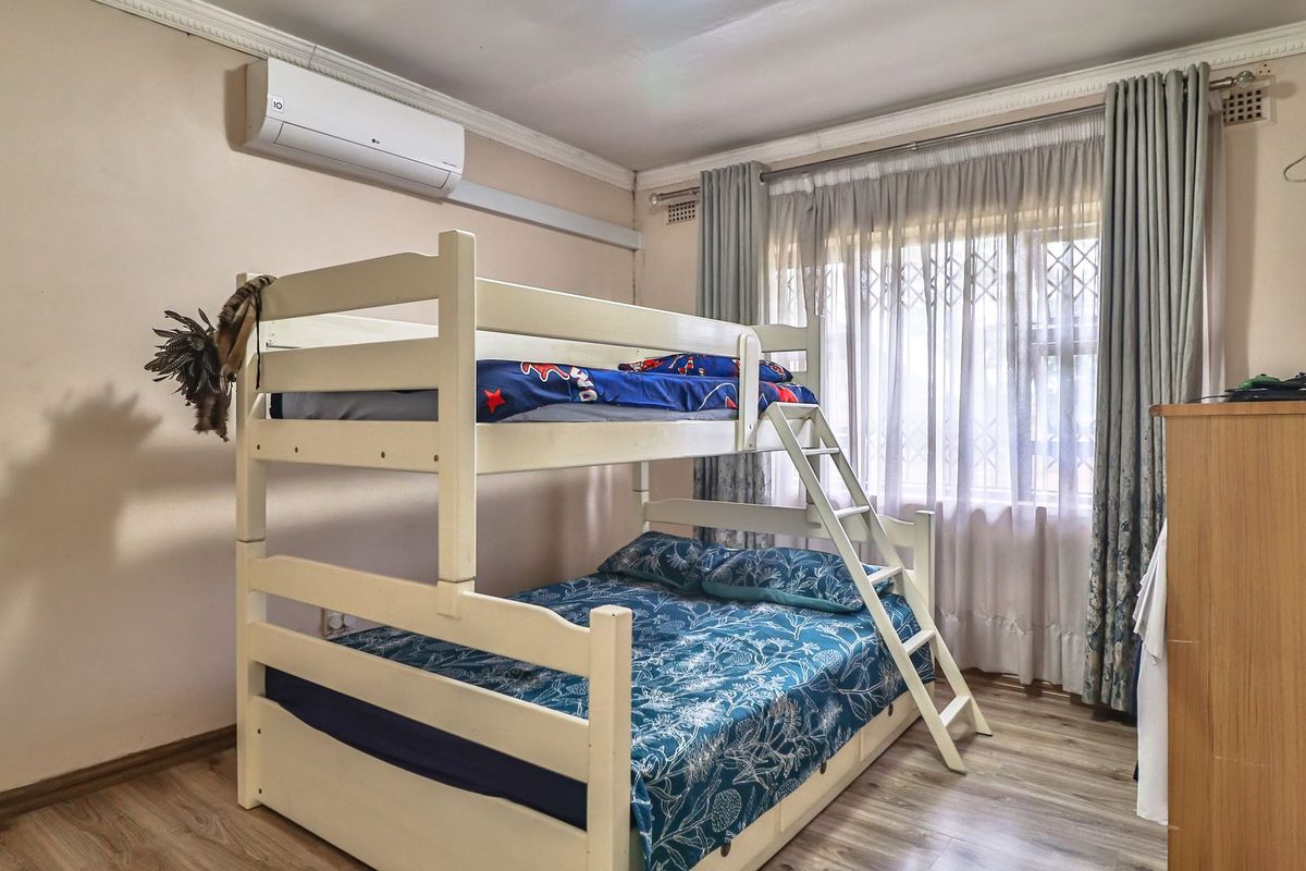 A bedroom featuring laminate flooring, a wall-mounted split-system air conditioner, and a window fitted with a security gate.