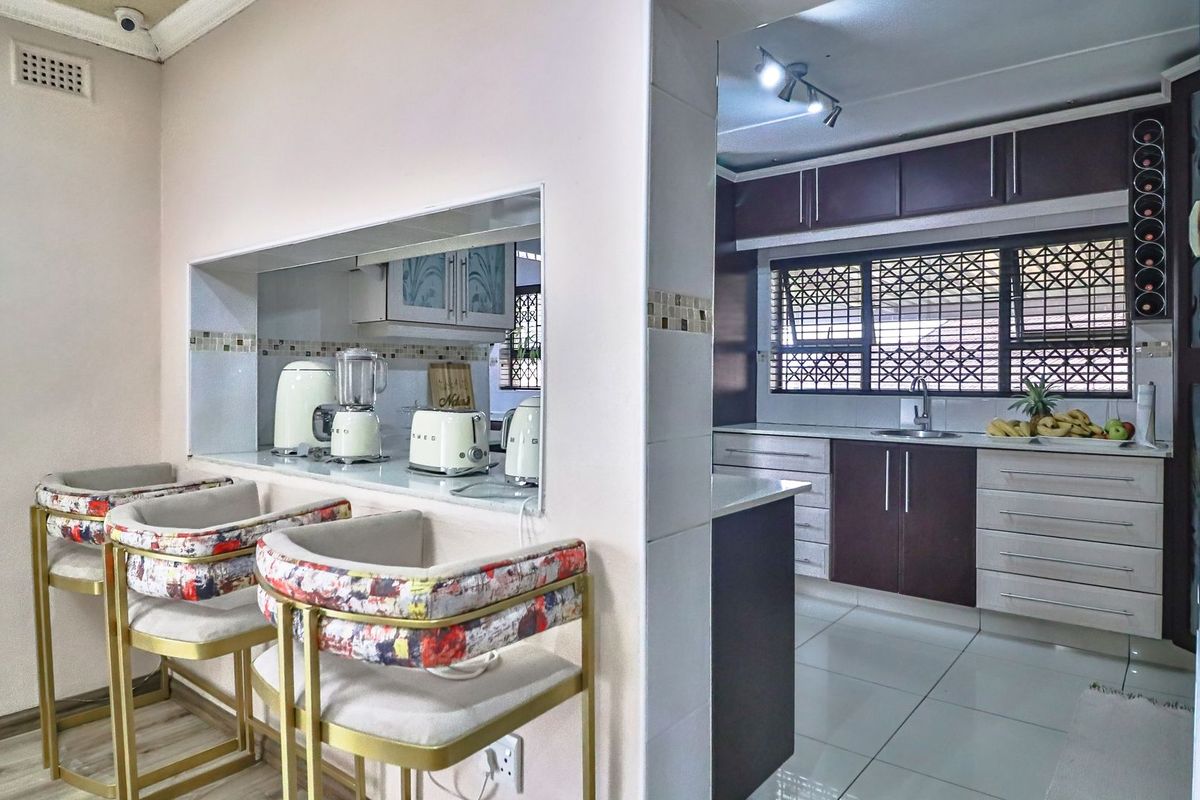 A functional kitchen featuring dark cabinetry, a breakfast bar pass-through, tiled flooring, and security bars on the windows.