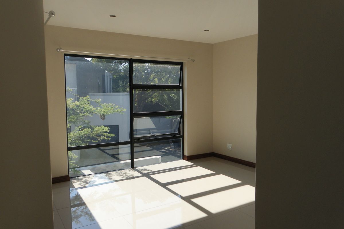 A bright, empty bedroom featuring large aluminium-framed windows, polished tiled flooring, and recessed downlighting, offering a clean and neutral space.