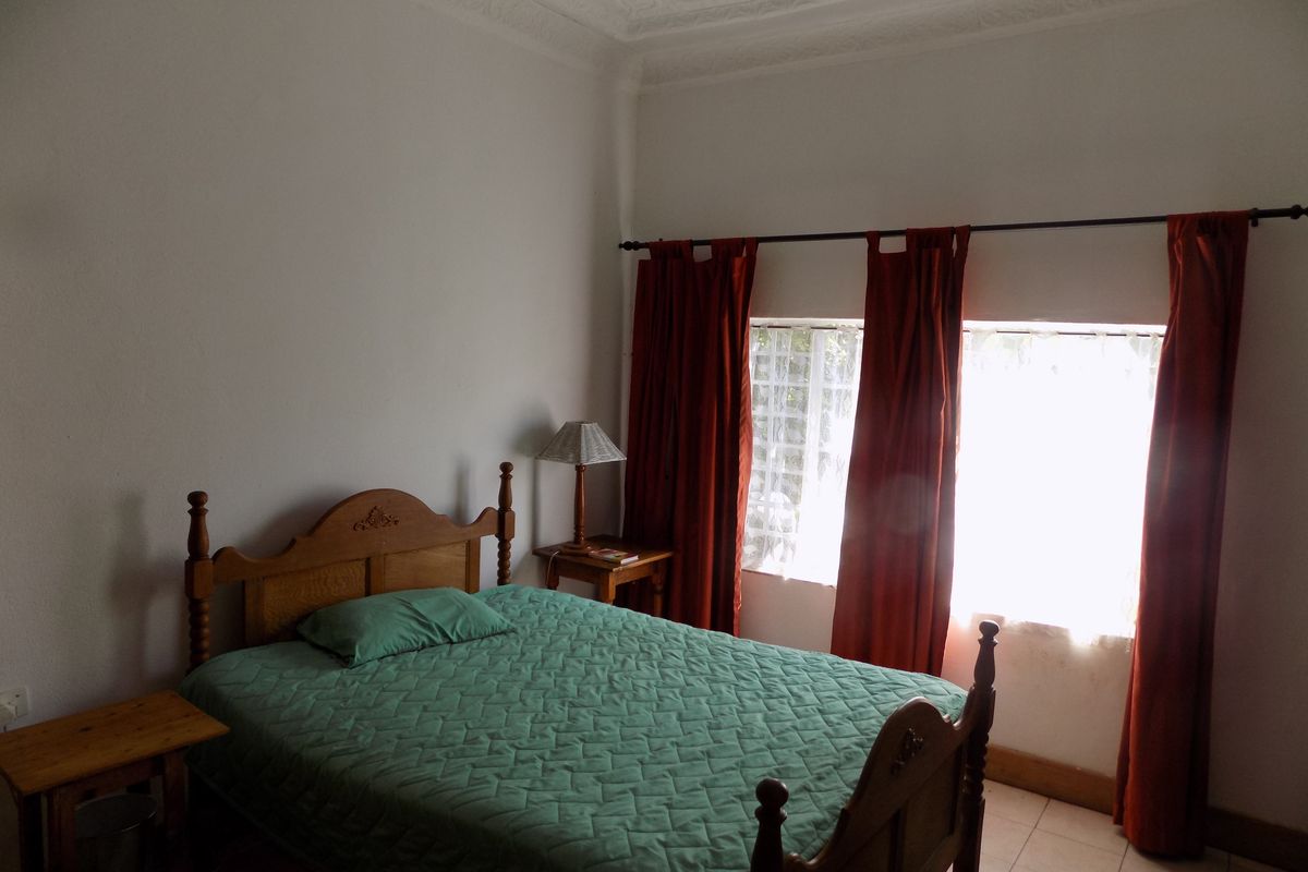 A bedroom featuring decorative ceiling cornicing, tiled flooring, and large windows with curtain rods.