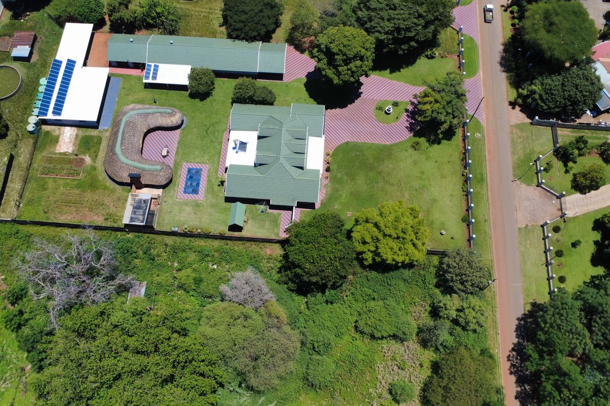 Aerial view of a large residential property featuring multiple buildings, solar installations, a swimming pool, and extensive landscaped grounds with paved access.