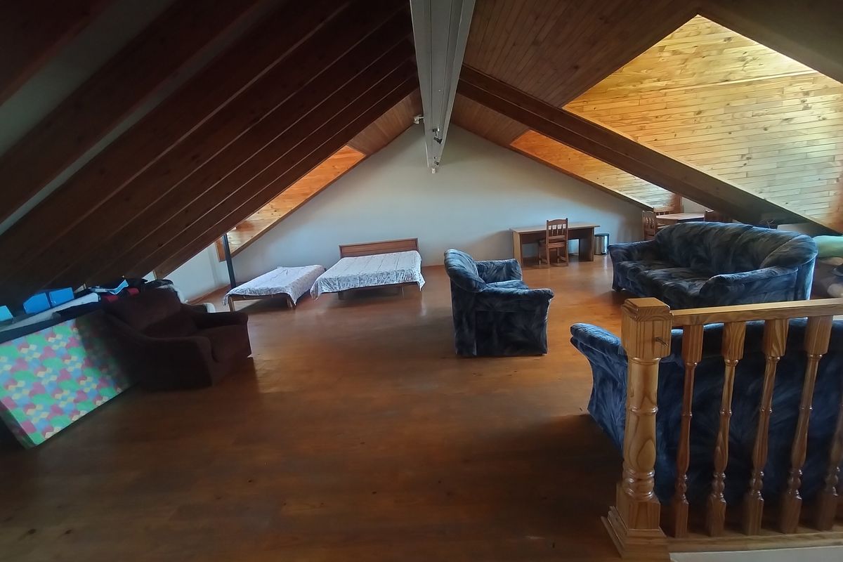 Spacious attic-style bedroom featuring exposed timber rafters, wood-paneled ceilings, and warm timber flooring, offering a unique and versatile living space.