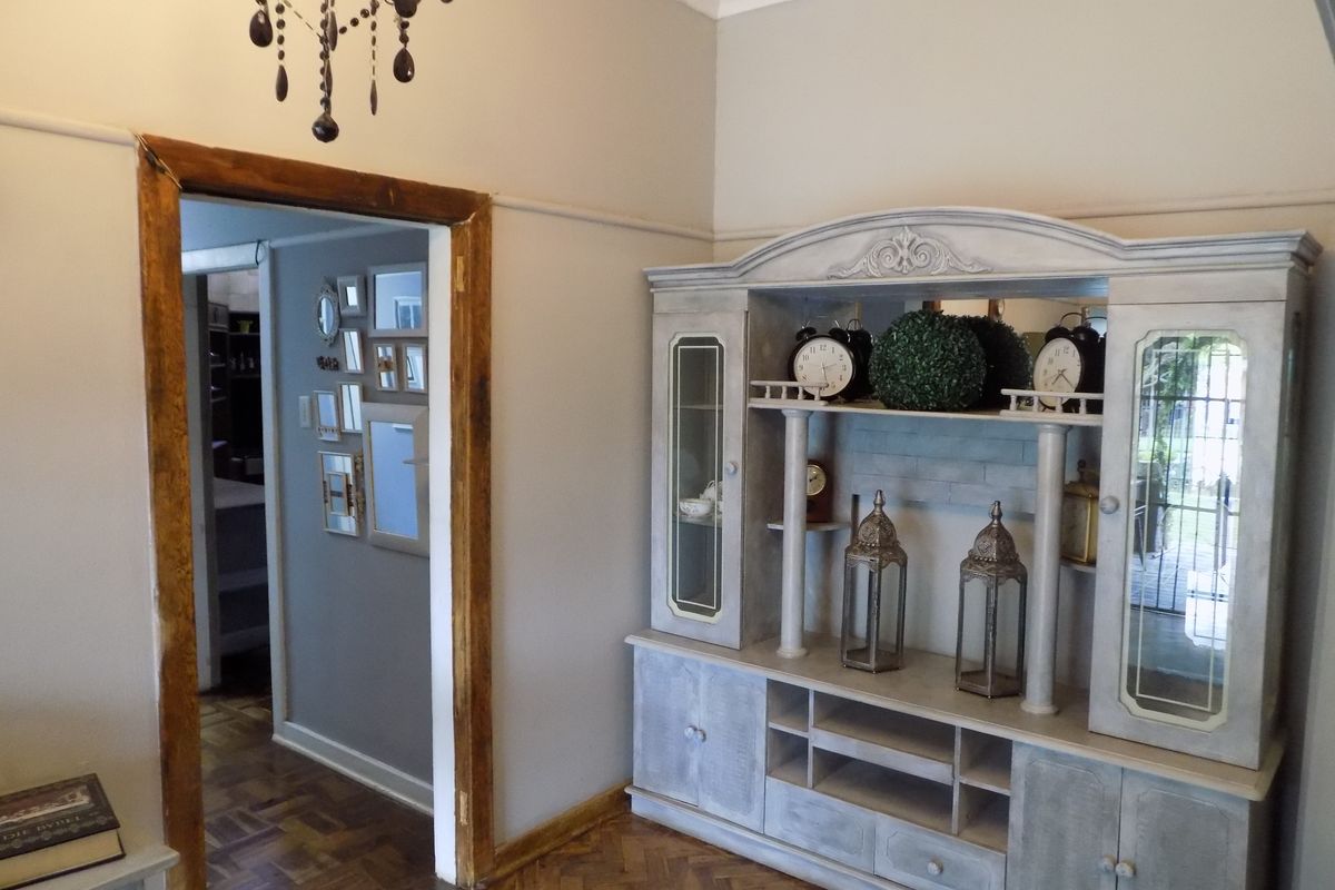 A living area featuring classic parquet flooring, neutral wall tones, and a decorative chandelier, with a doorway leading to an adjacent room.