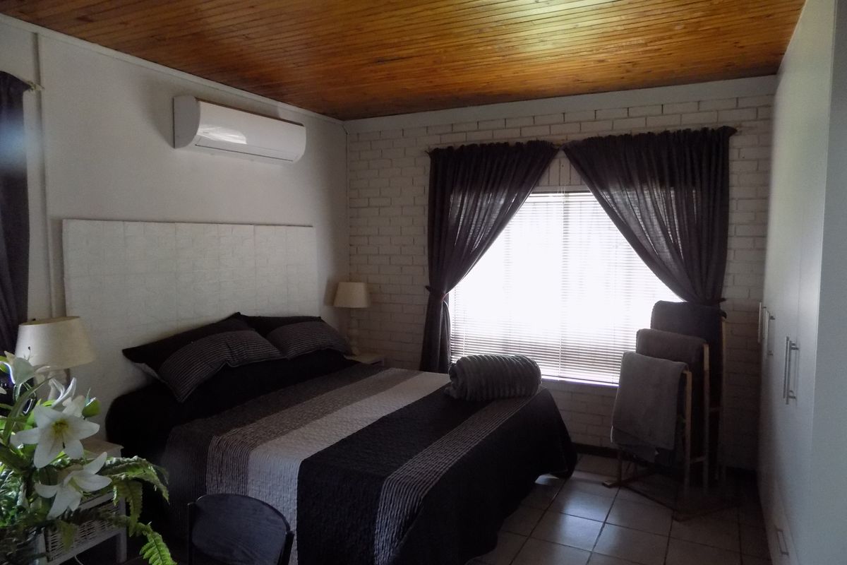 A bedroom featuring a timber-clad ceiling, painted brick feature wall, tiled flooring, and a wall-mounted air conditioning unit.