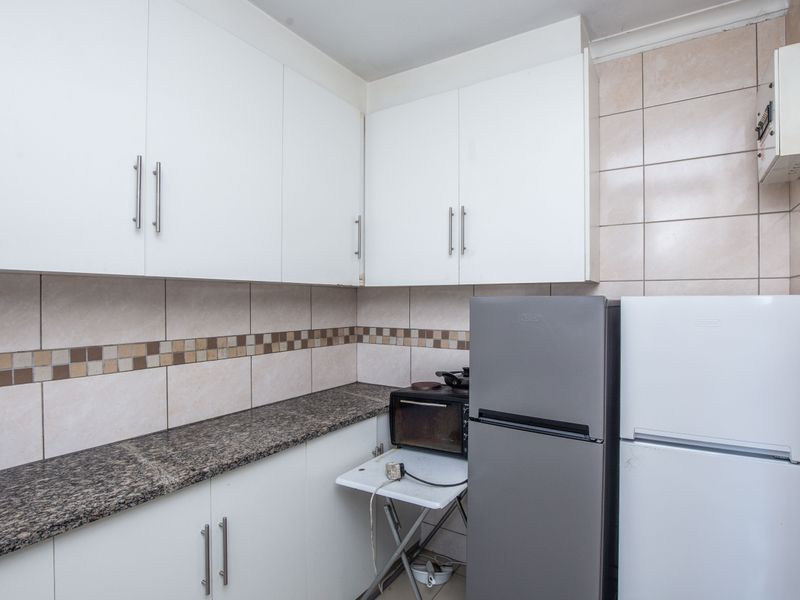 Compact kitchen featuring white cabinetry, granite countertops, and a tiled backsplash, providing functional storage and preparation space.