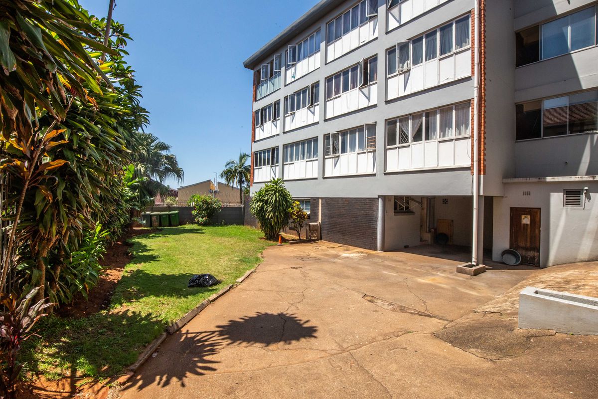 Rear view of the apartment building featuring a concrete driveway, lawn area, and multi-story facade with casement windows.