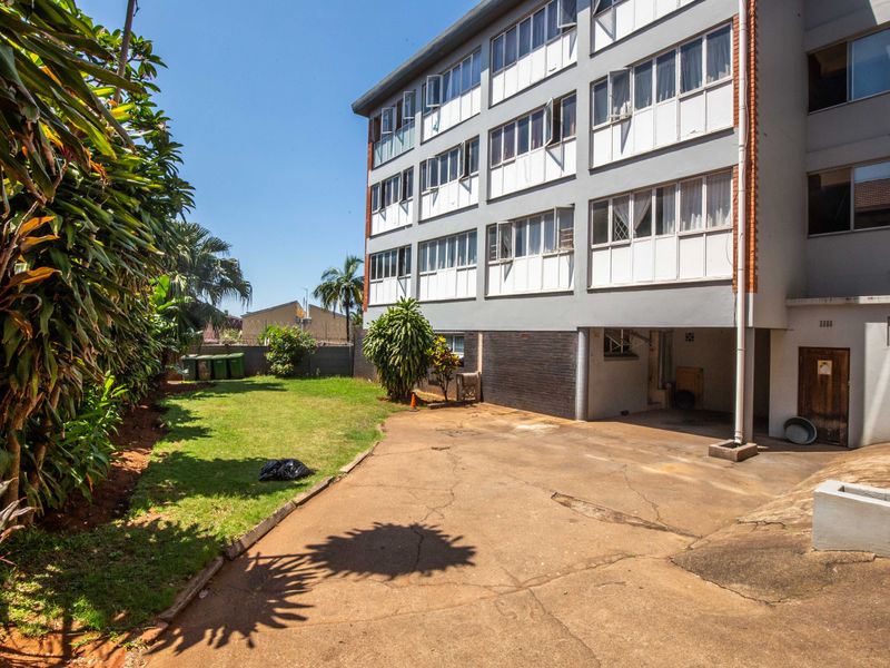 Rear view of the apartment building featuring a concrete driveway, lawn area, and multi-story facade with casement windows.