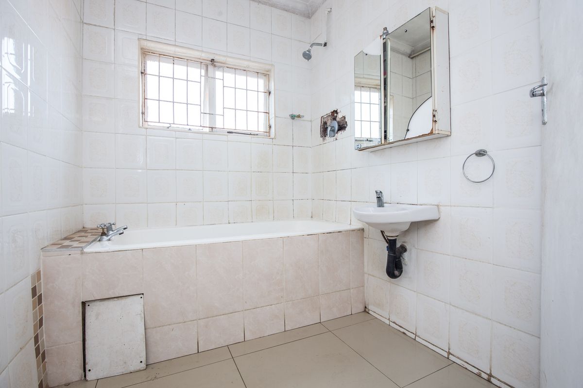 A dated bathroom featuring a bathtub, wall-mounted basin, and tiled finishes, currently requiring renovation and repair to the wall and cabinetry.