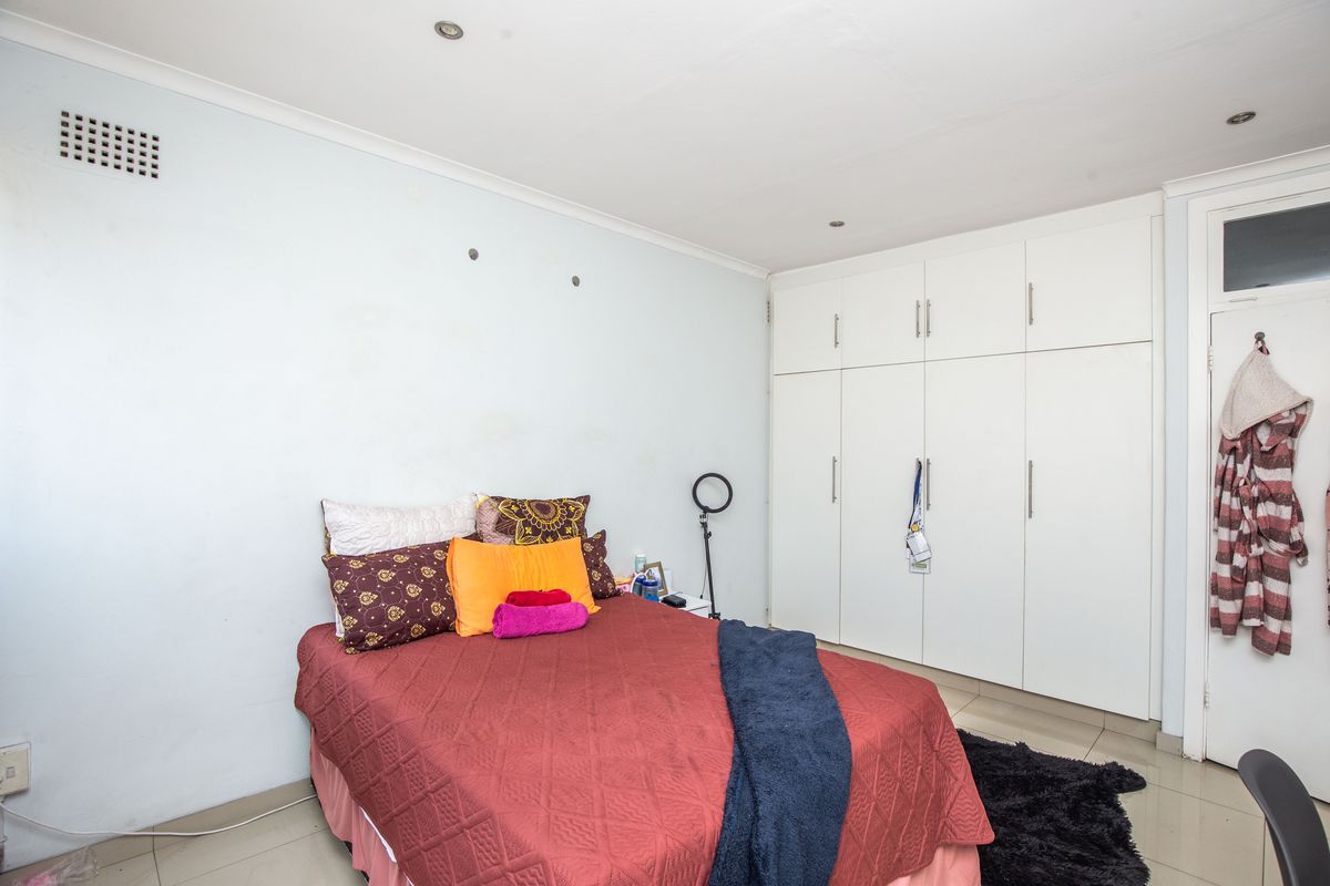 A bedroom featuring built-in white cupboards, recessed downlighting, and tiled flooring.