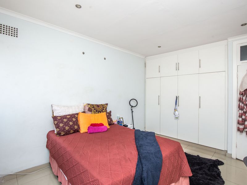 A bedroom featuring built-in white cupboards, recessed downlighting, and tiled flooring.