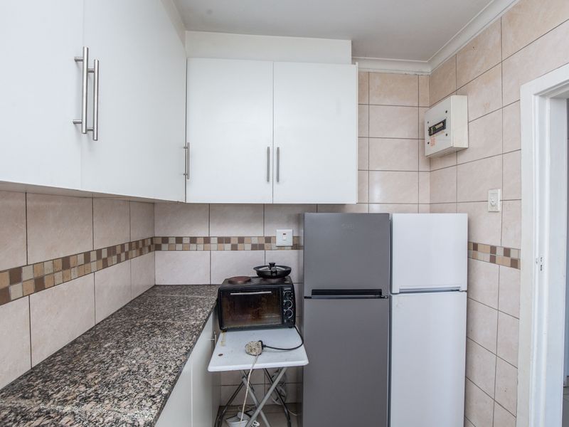 Compact kitchen featuring granite countertops, tiled backsplash, and white cabinetry, providing a functional space with potential for cosmetic updates.